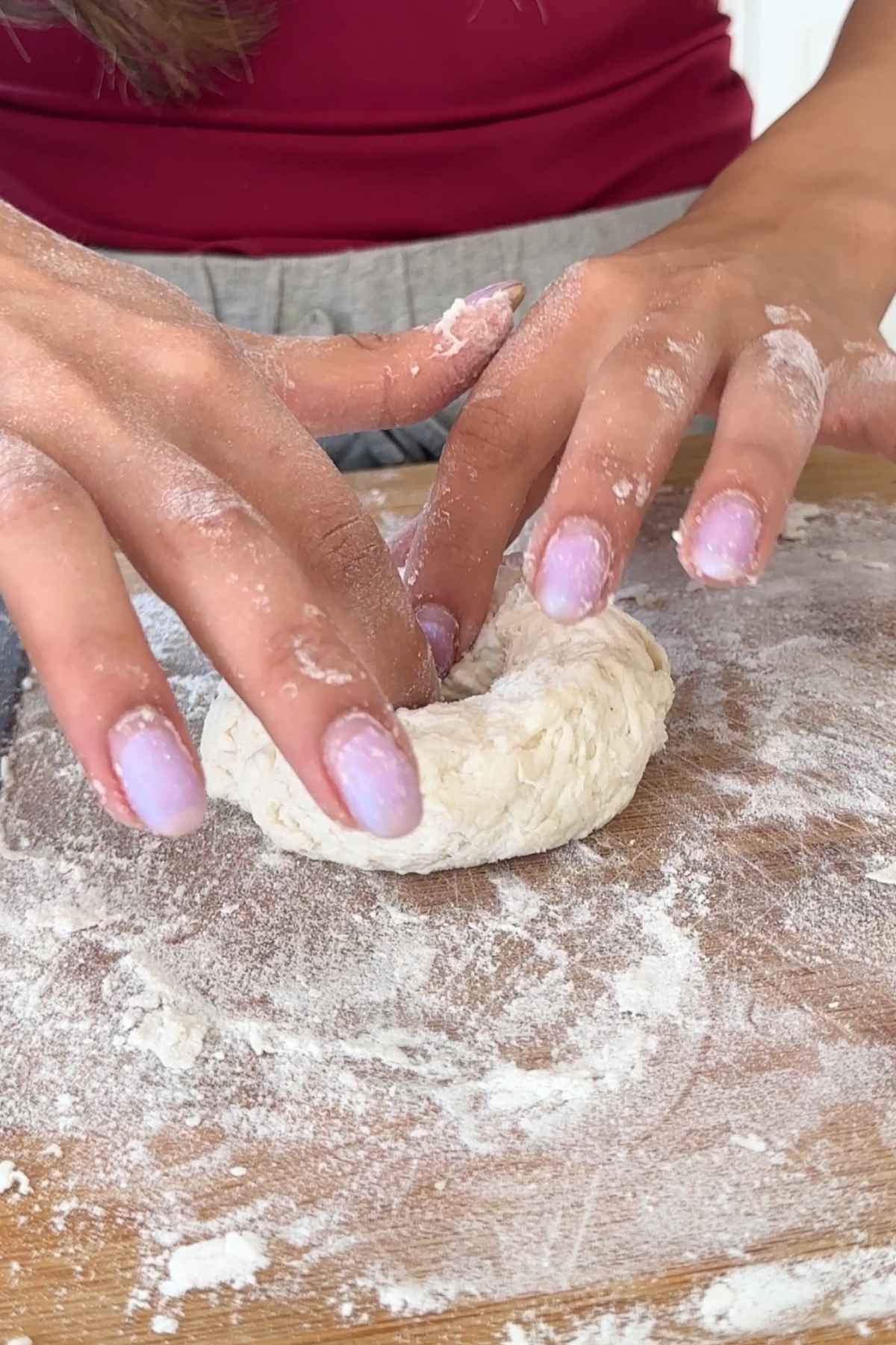 Hands shaping bagel dough on floured board.