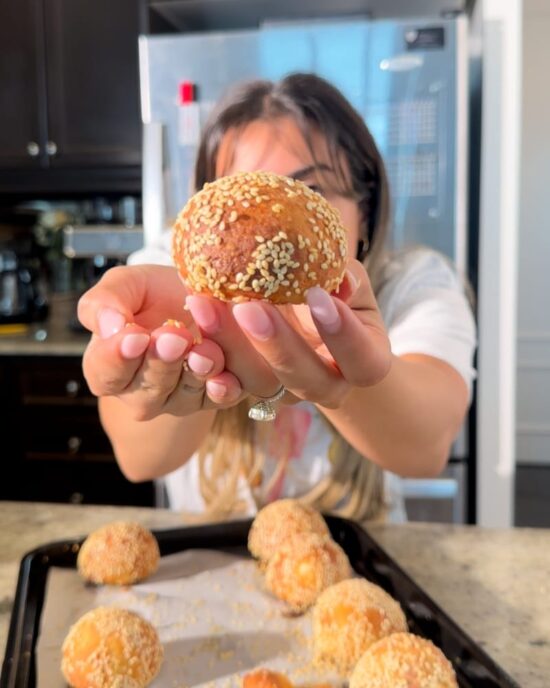 Woman holding a high protein bagel bite covered in sesame seeds, with more bagel bites on a tray.