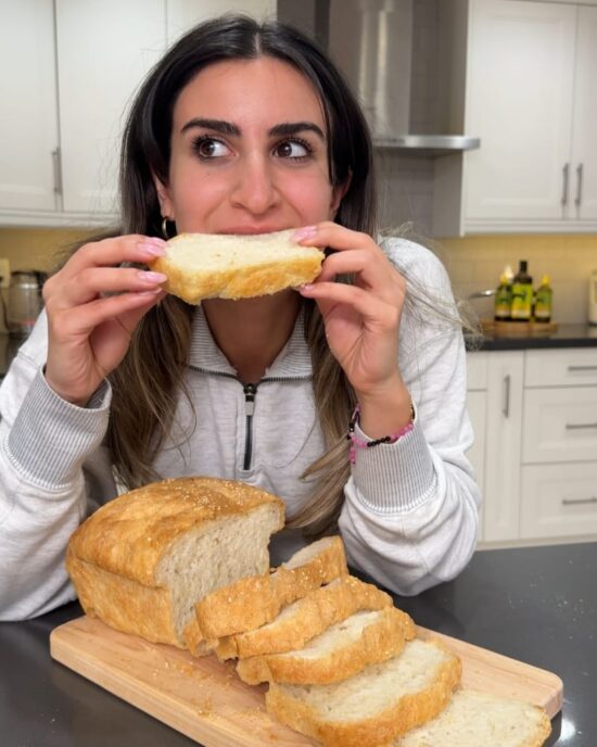 Woman taking a bite of homemade sandwich bread. Freshly baked bread slices on a wooden board.