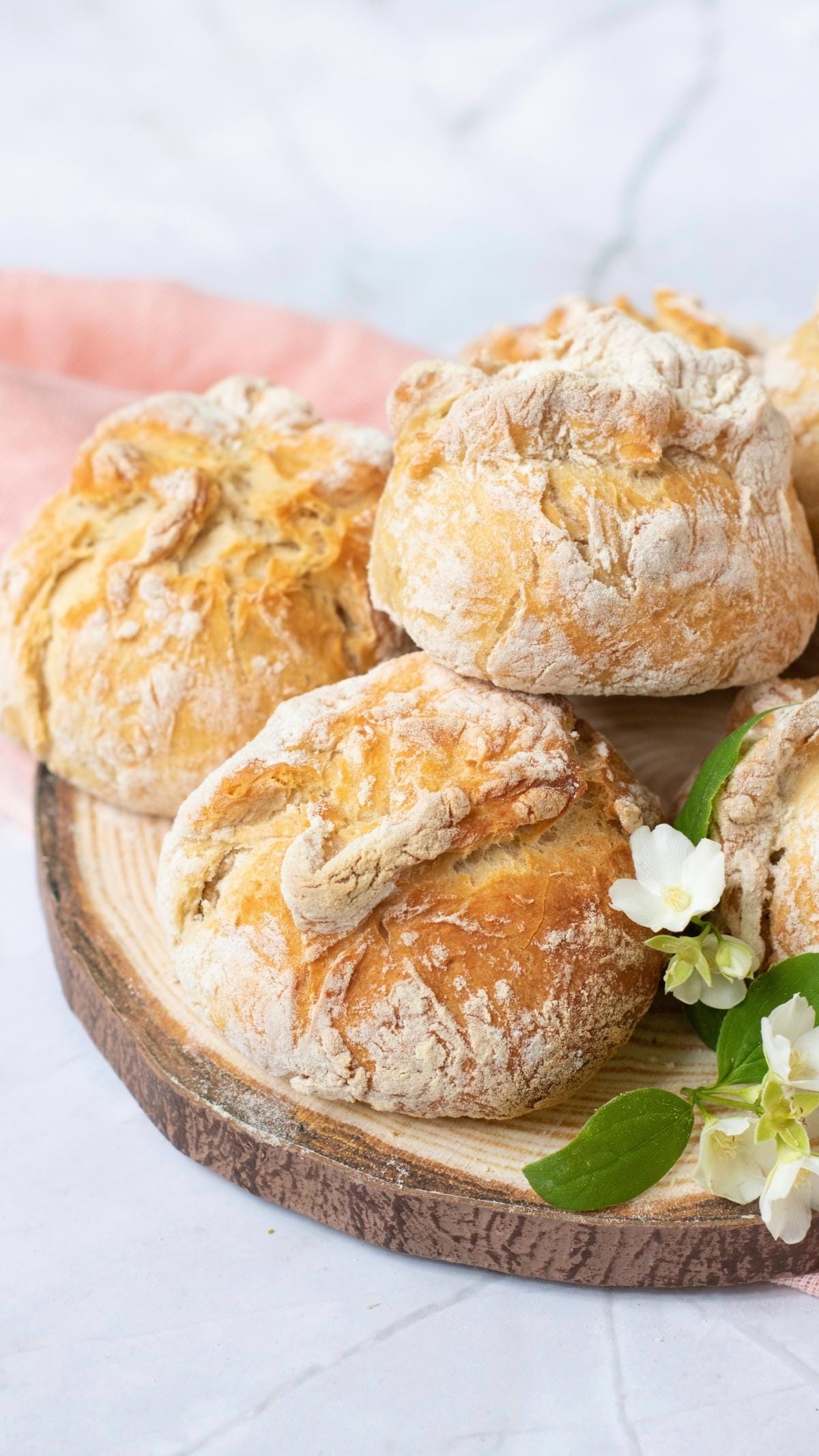 Freshly baked easy artisan bread rolls on a wooden board with white flowers and a pink cloth.