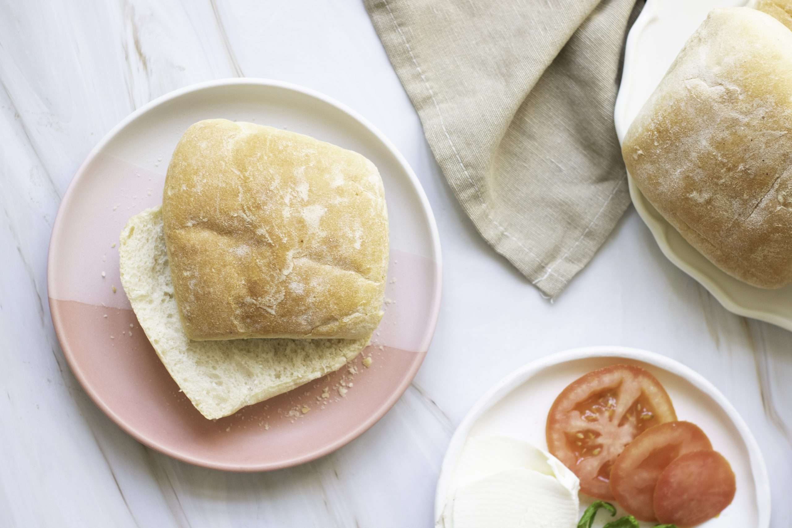 Ciabatta roll halves on plate, ready for filling with tomato and mozzarella. Quick Ciabatta bread rolls recipe.