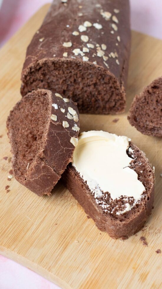Sliced chocolate brown bread with butter on a wooden board, perfect for a Copycat Cheesecake Factory Brown Bread recipe.