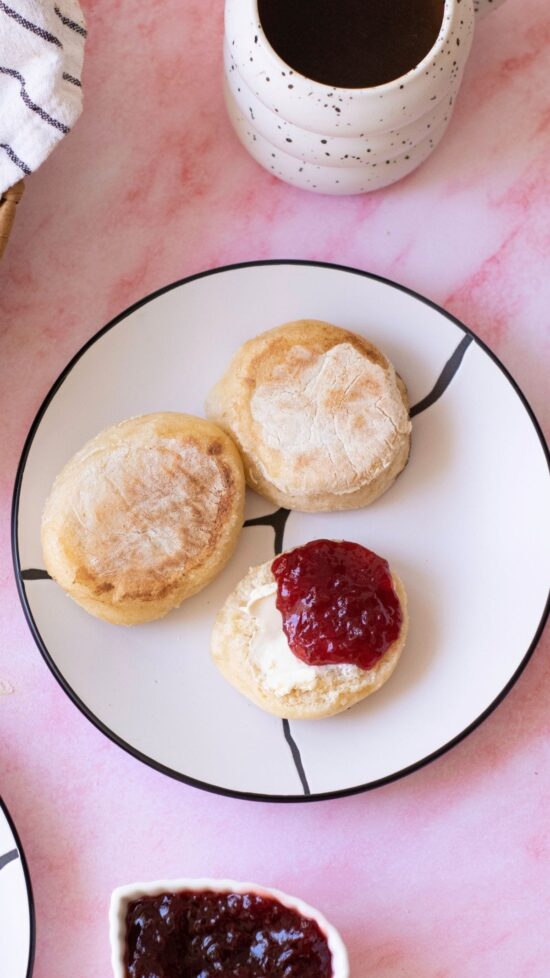 Homemade English muffins with butter and jam on a plate, ready to eat.