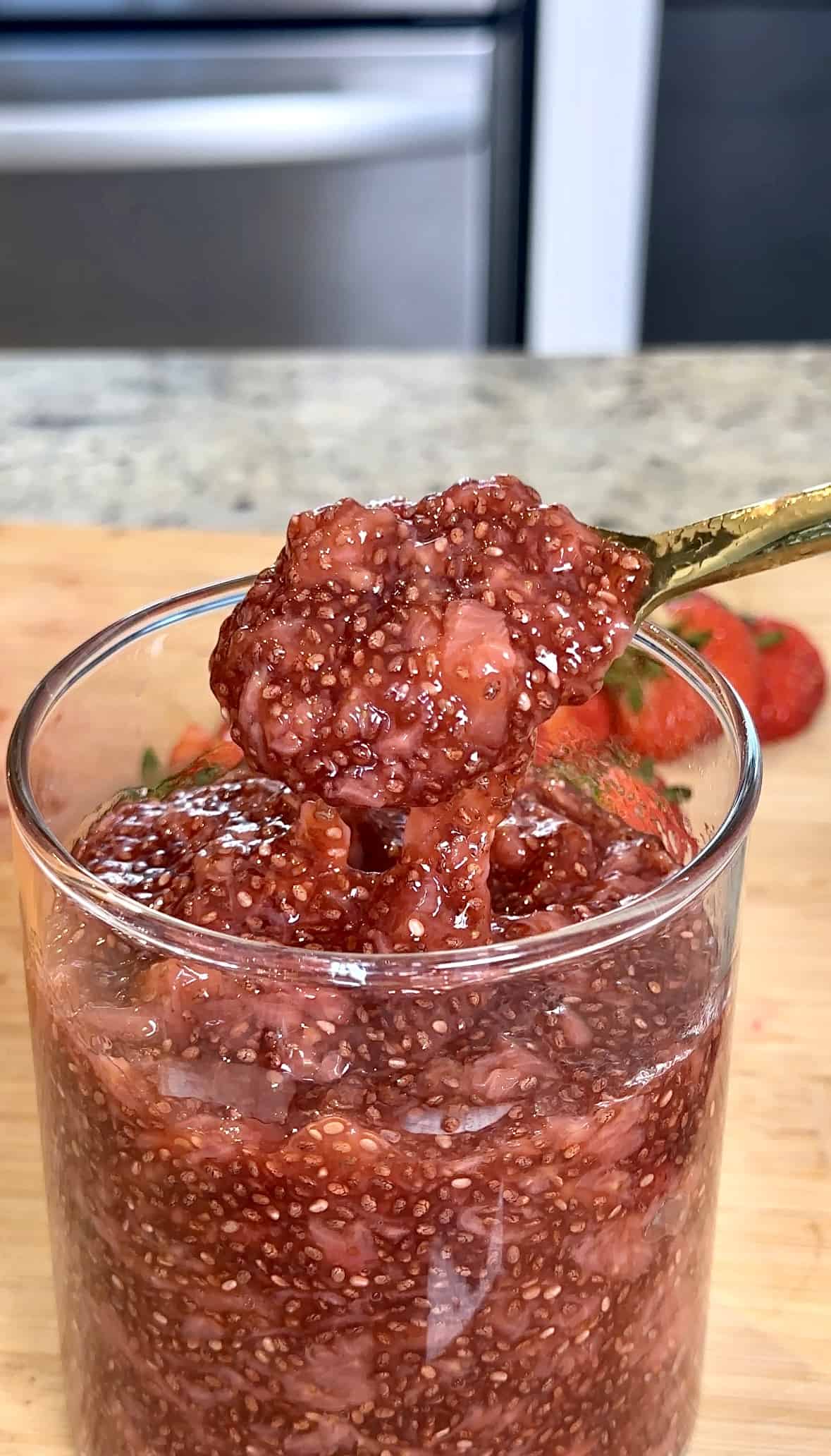 Close-up of strawberry chia seed jam in a glass, spoon holding a dollop. 4 Ingredient Strawberry Chia Seed Jam.