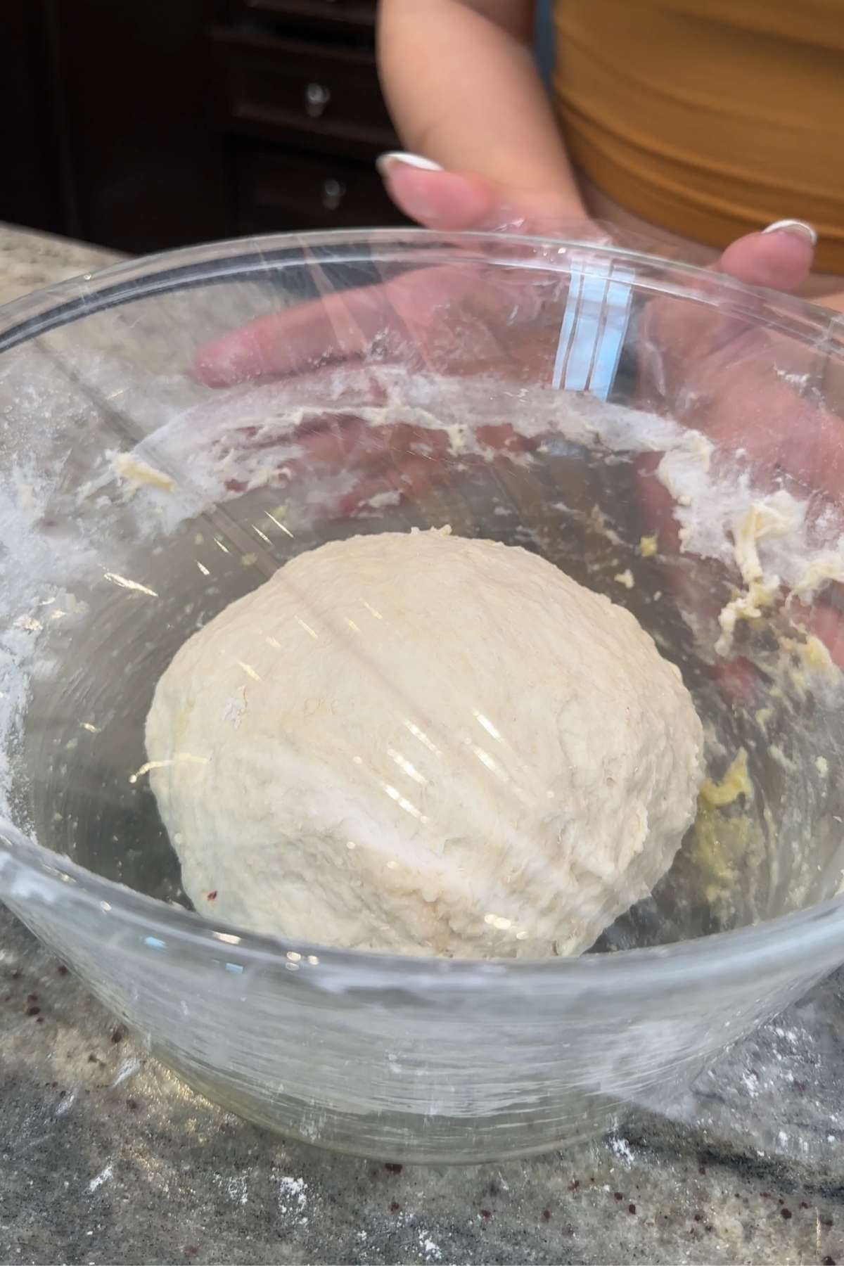 Dough ball covered in plastic wrap in a bowl.