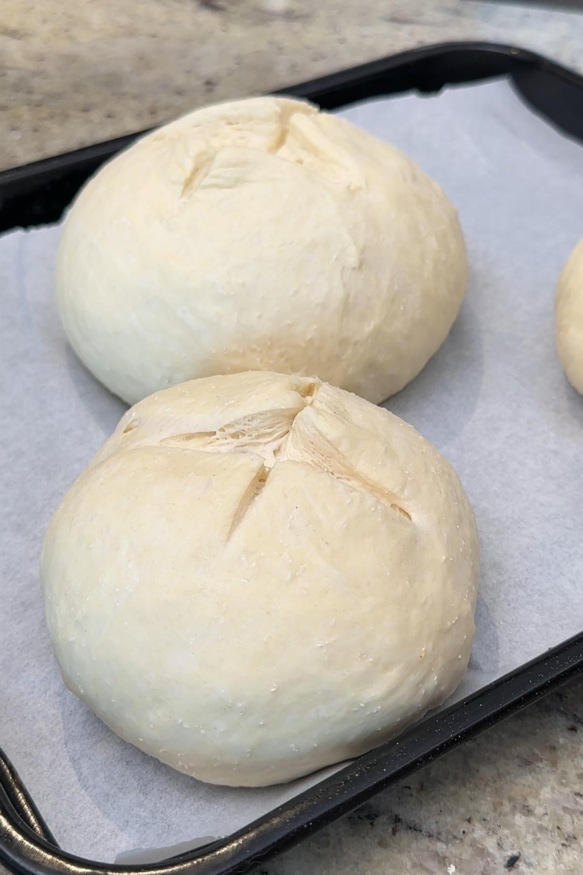 Two raw bread bowls on baking sheet.