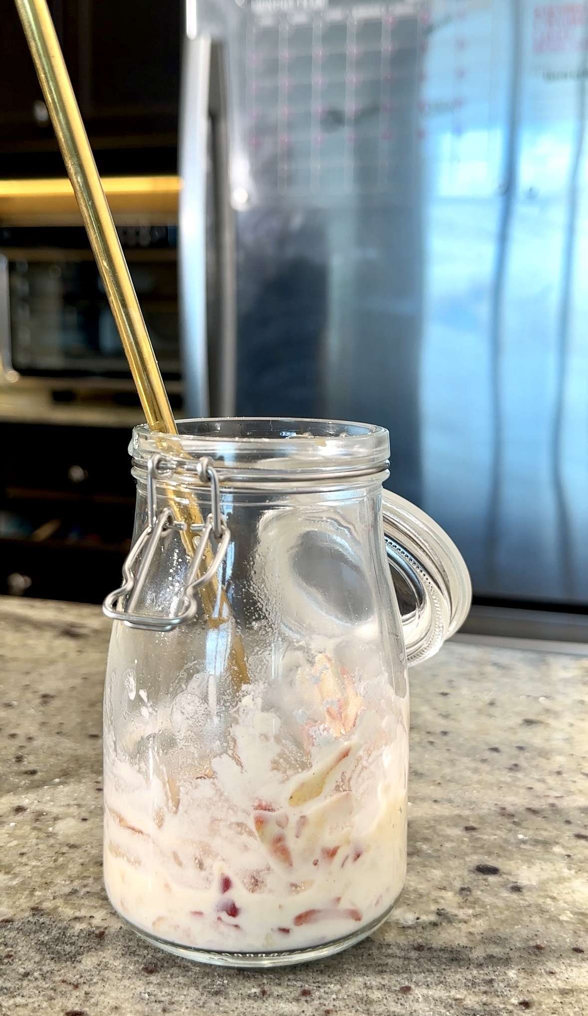 Glass jar with remnants of apple mixture, sourdough starter, and a gold straw on a counter.