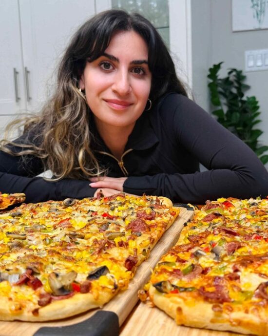 Woman smiles over two large pizzas, made with easy same day pizza dough recipe.
