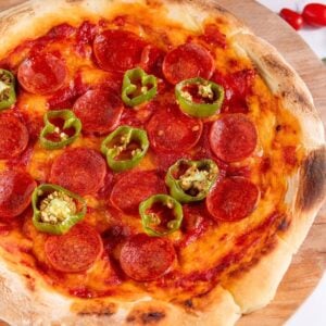Pepperoni and jalapeño pizza on wooden board.