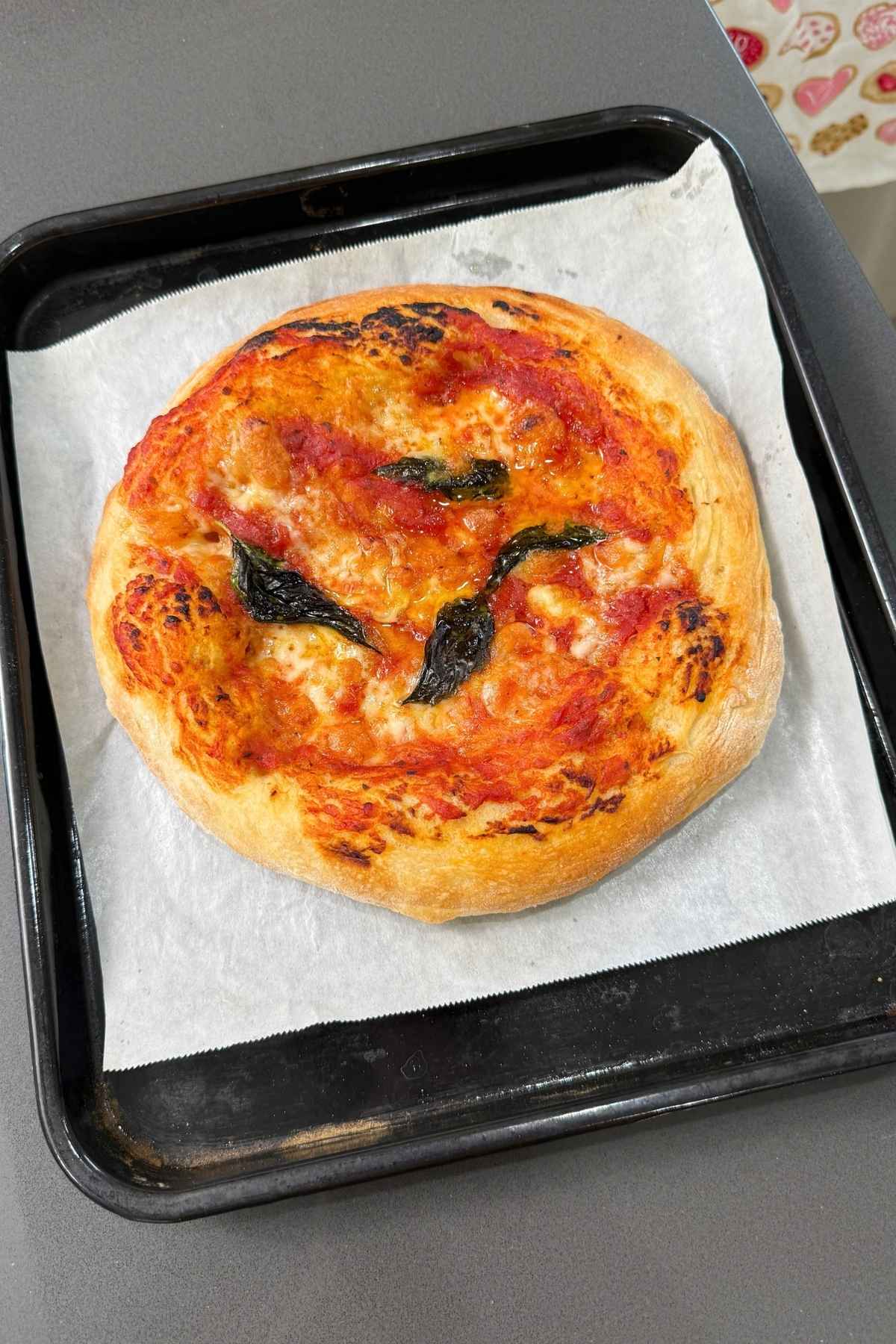 Neapolitan pizza with basil on baking sheet.