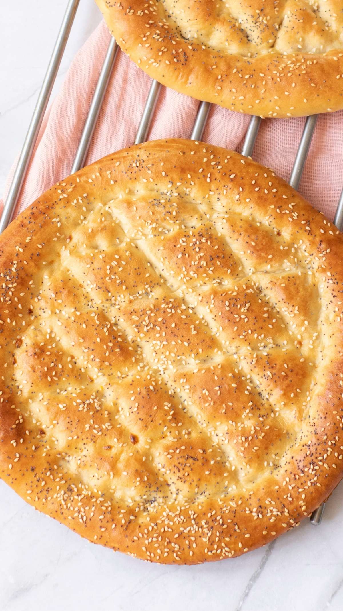 Close-up of round Turkish bread with sesame seeds, cooling on a rack.