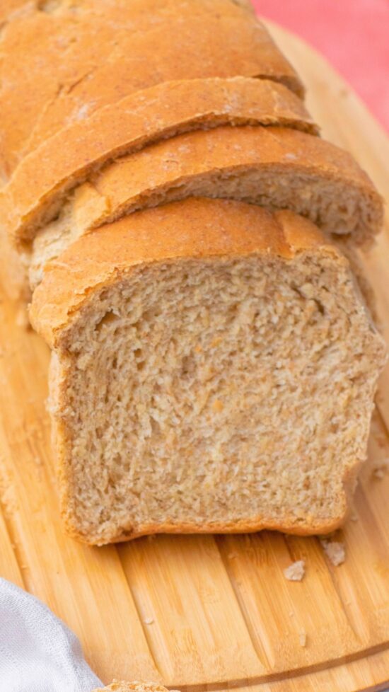 Sliced homemade whole wheat bread on a wooden cutting board, ready to eat.