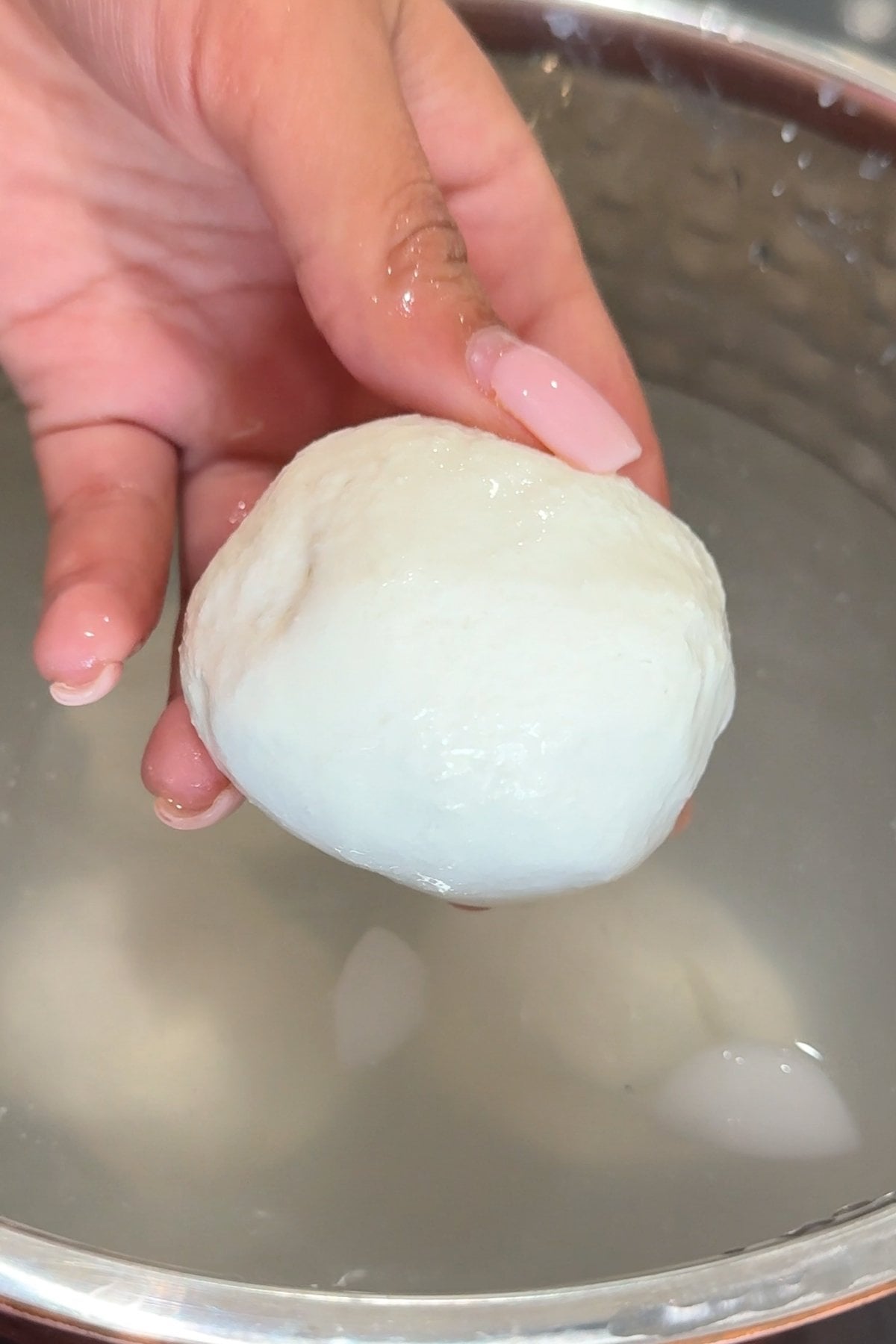 Hand holding mozzarella ball over water