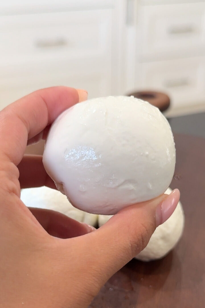 Hand holding homemade mozzarella ball, fresh cheese recipe