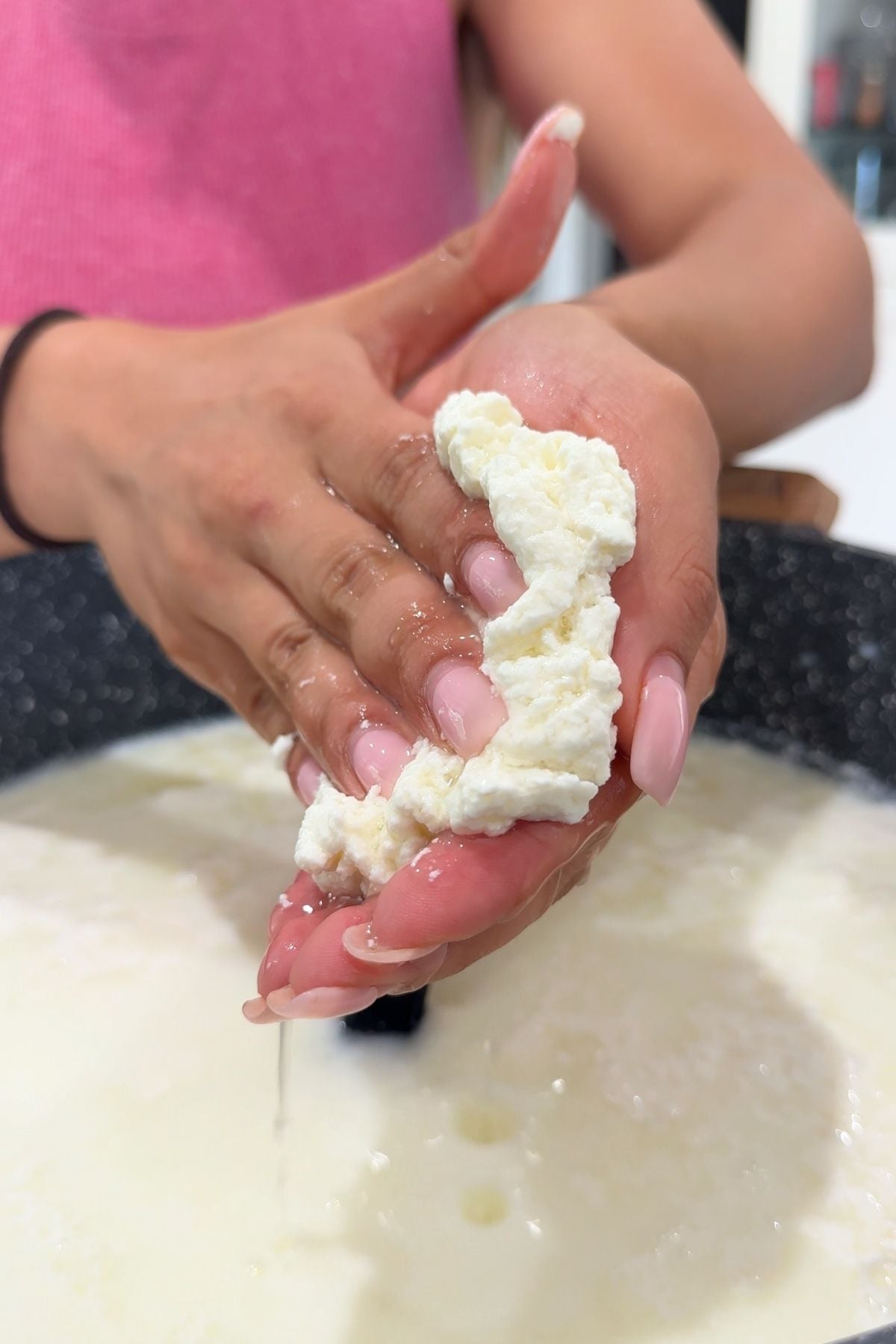 Hands squeezing mozzarella curds over pot