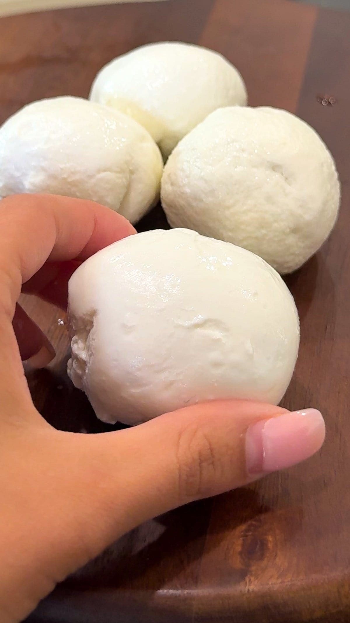 Hand holding fresh mozzarella cheese balls on a wooden board. Learn how to make mozzarella cheese!