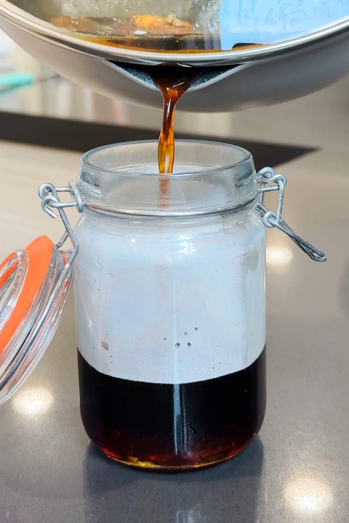 Pouring dark syrup into jar with foam.