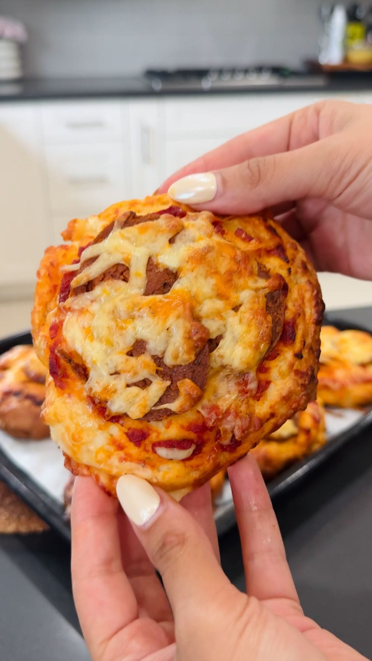 Close-up of a cheesy pizza biscuit bite held in hands, fresh from the oven.