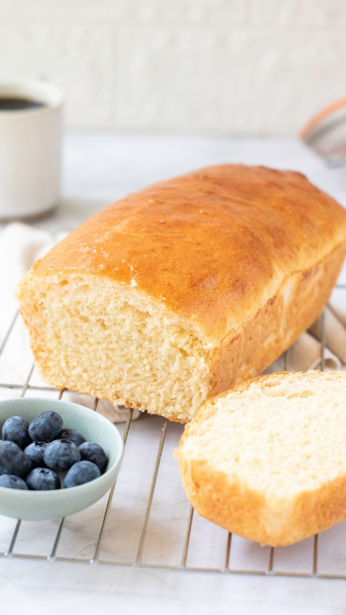 Freshly baked loaf of sandwich bread with a slice cut, served with blueberries and coffee.