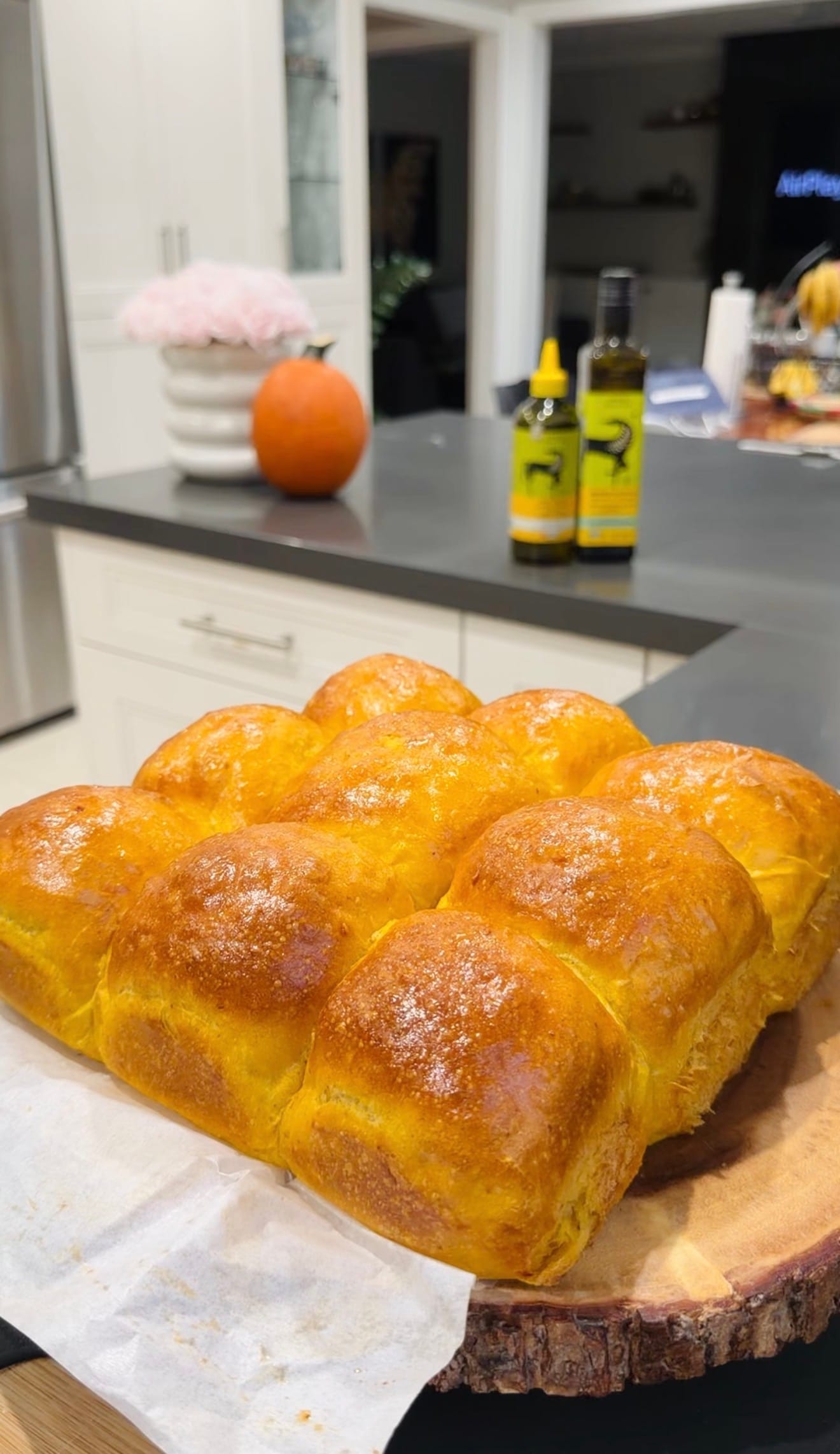 Freshly baked pumpkin dinner rolls on parchment paper and a wood board.