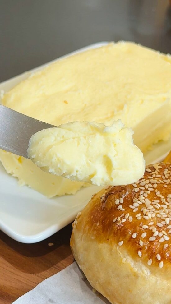 Homemade butter on a knife about to be spread on a sesame seed bun.