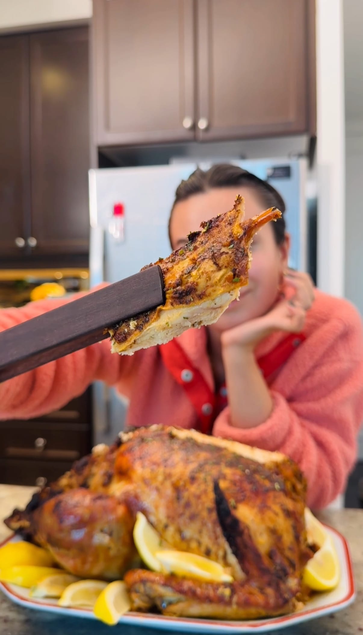 Woman holding a slice of golden brown Thanksgiving turkey with lemon garnish, ready to eat.