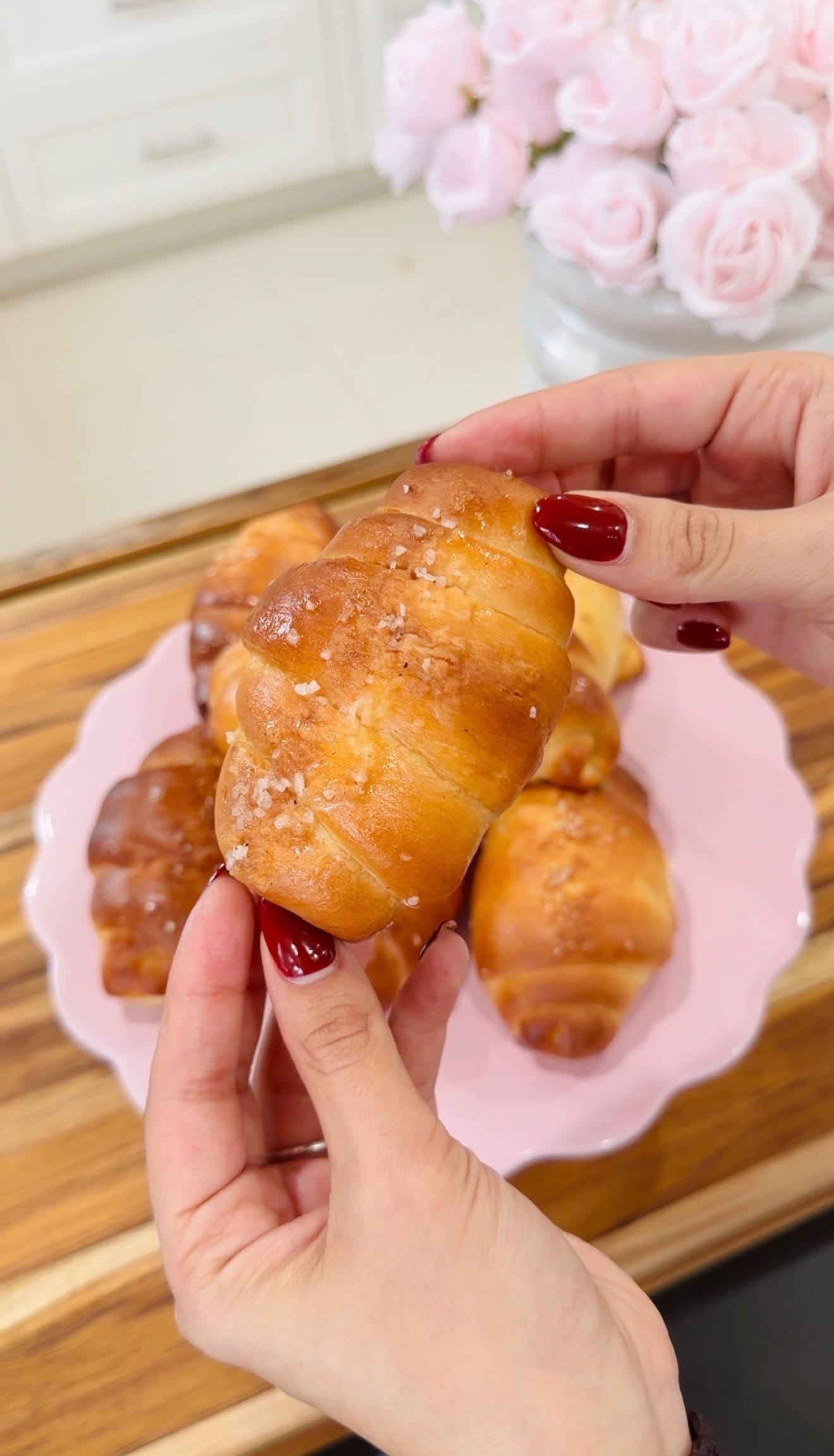 Hands holding freshly baked salt bread roll, pink plate of rolls, roses