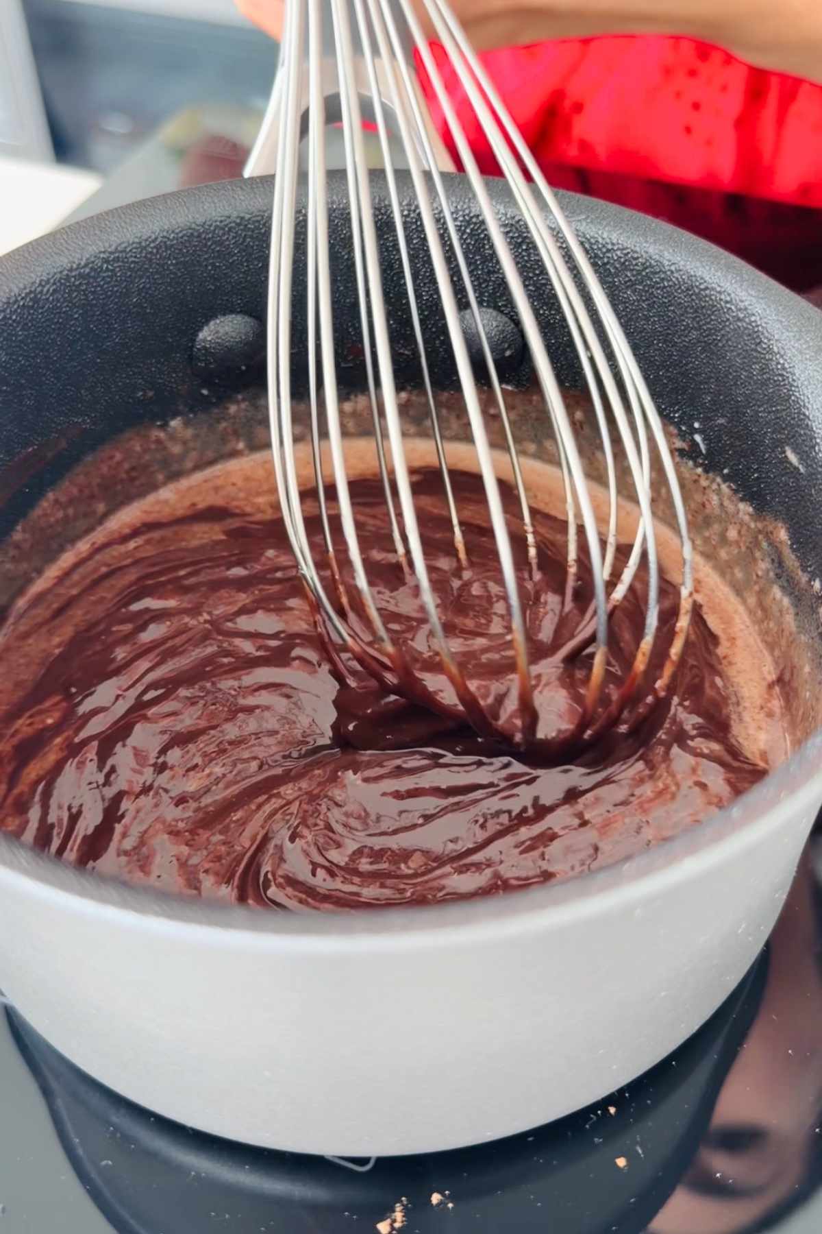 Whisk mixing rich chocolate batter in pot.