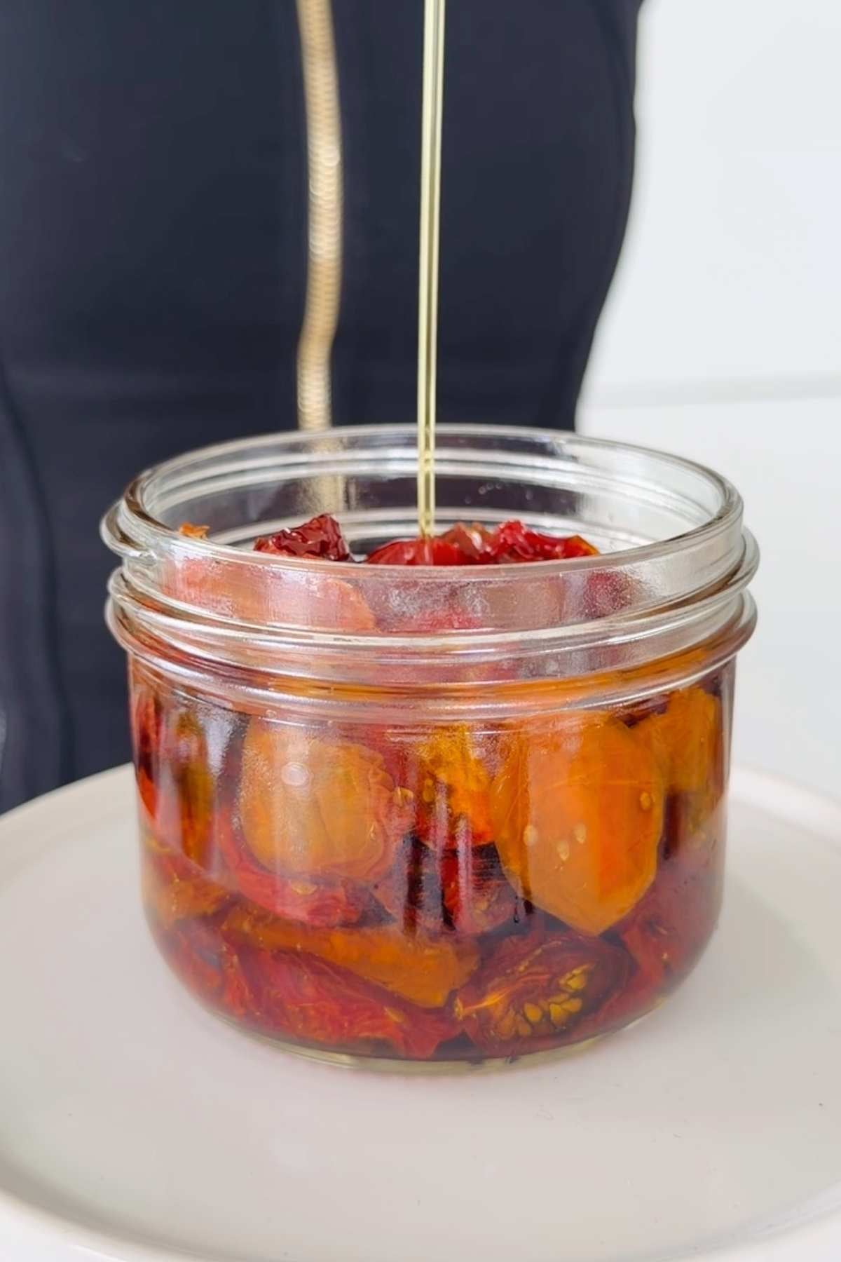 Jar of homemade sundried tomatoes being drizzled with oil.